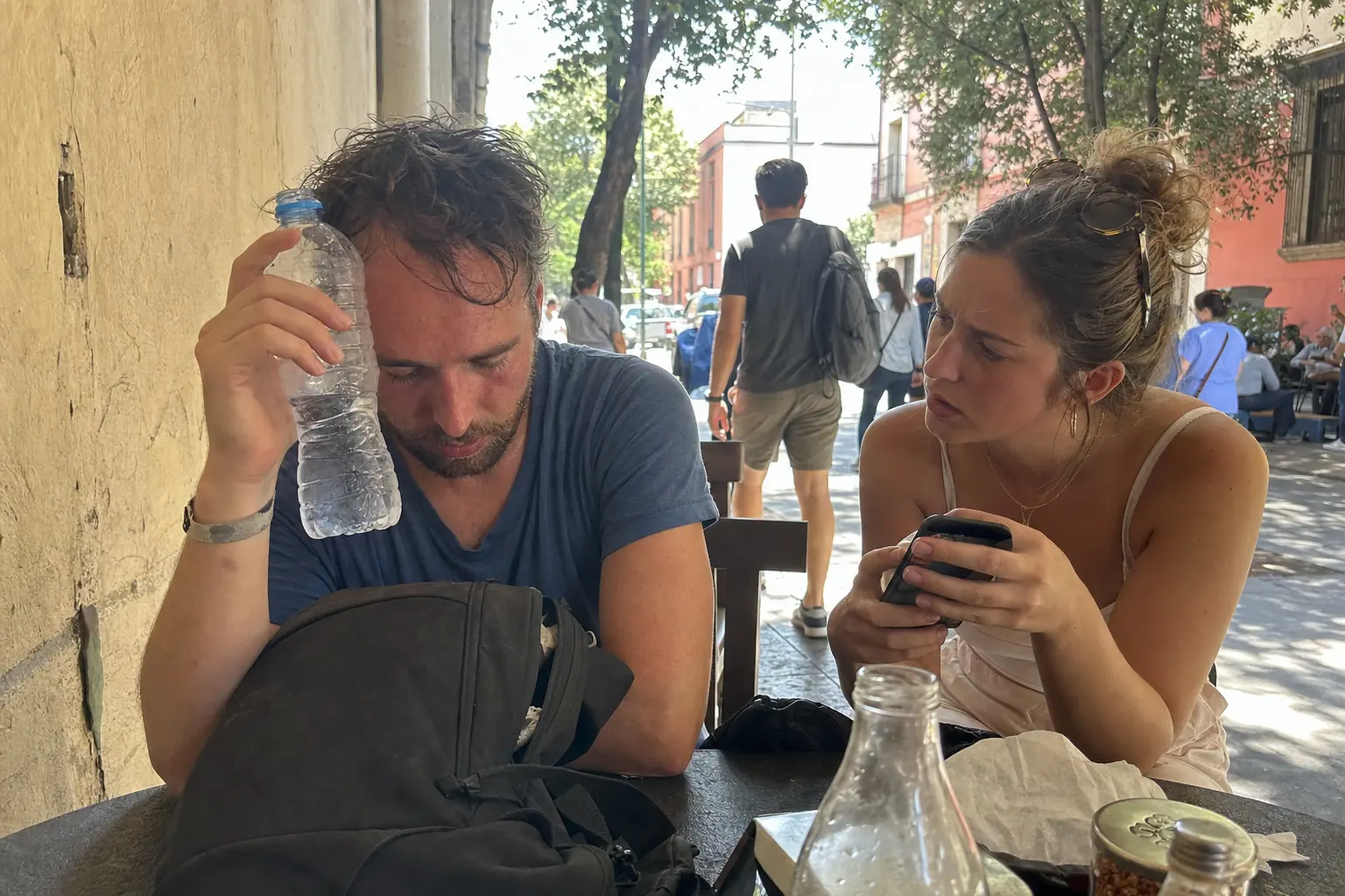 Candid phone photo of a dehydrated traveler resting at a Mexico City cafe table while a friend uses a phone.