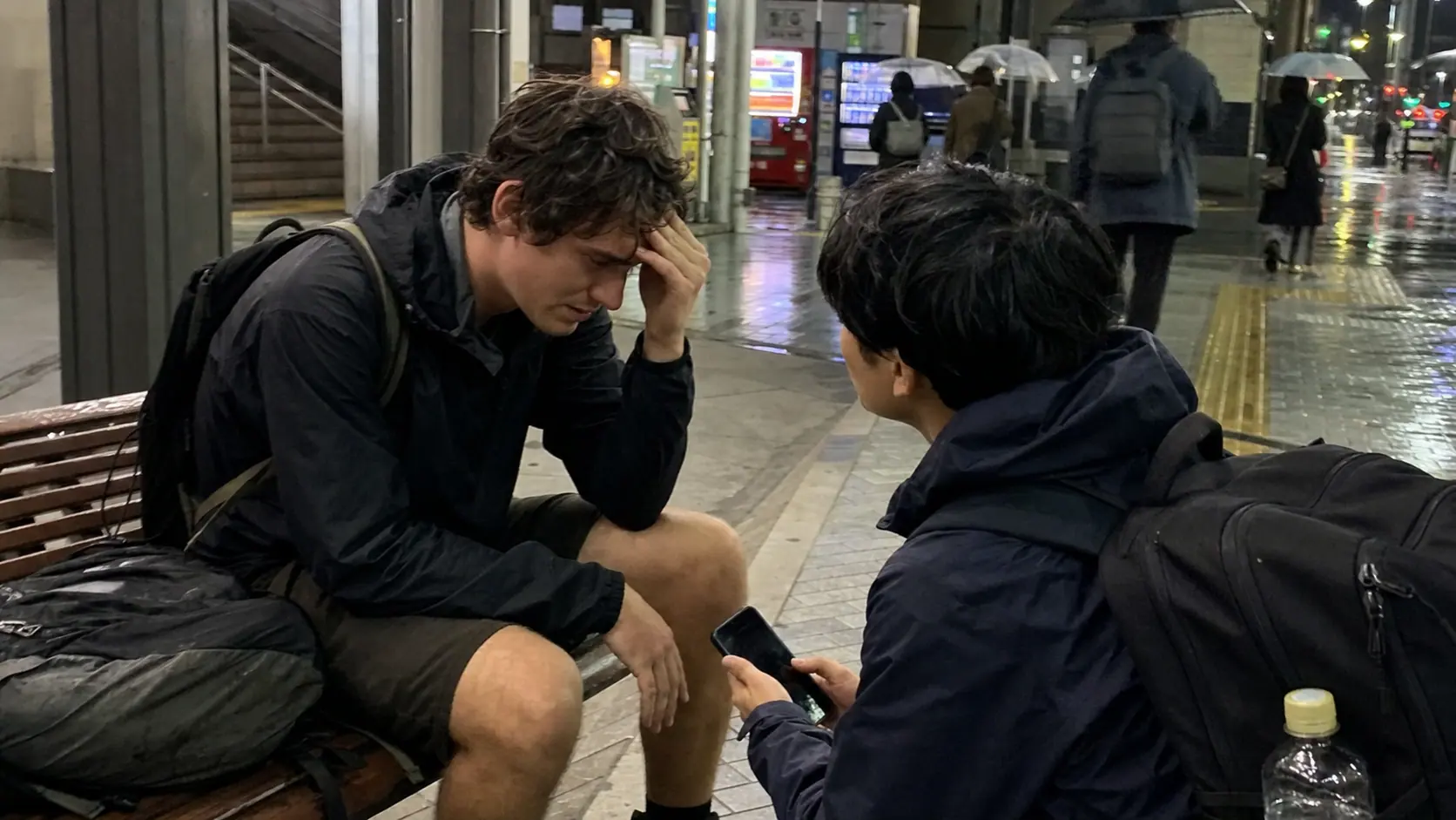 Candid phone photo of a traveler sitting after a fall near a rainy Tokyo street or station entrance.